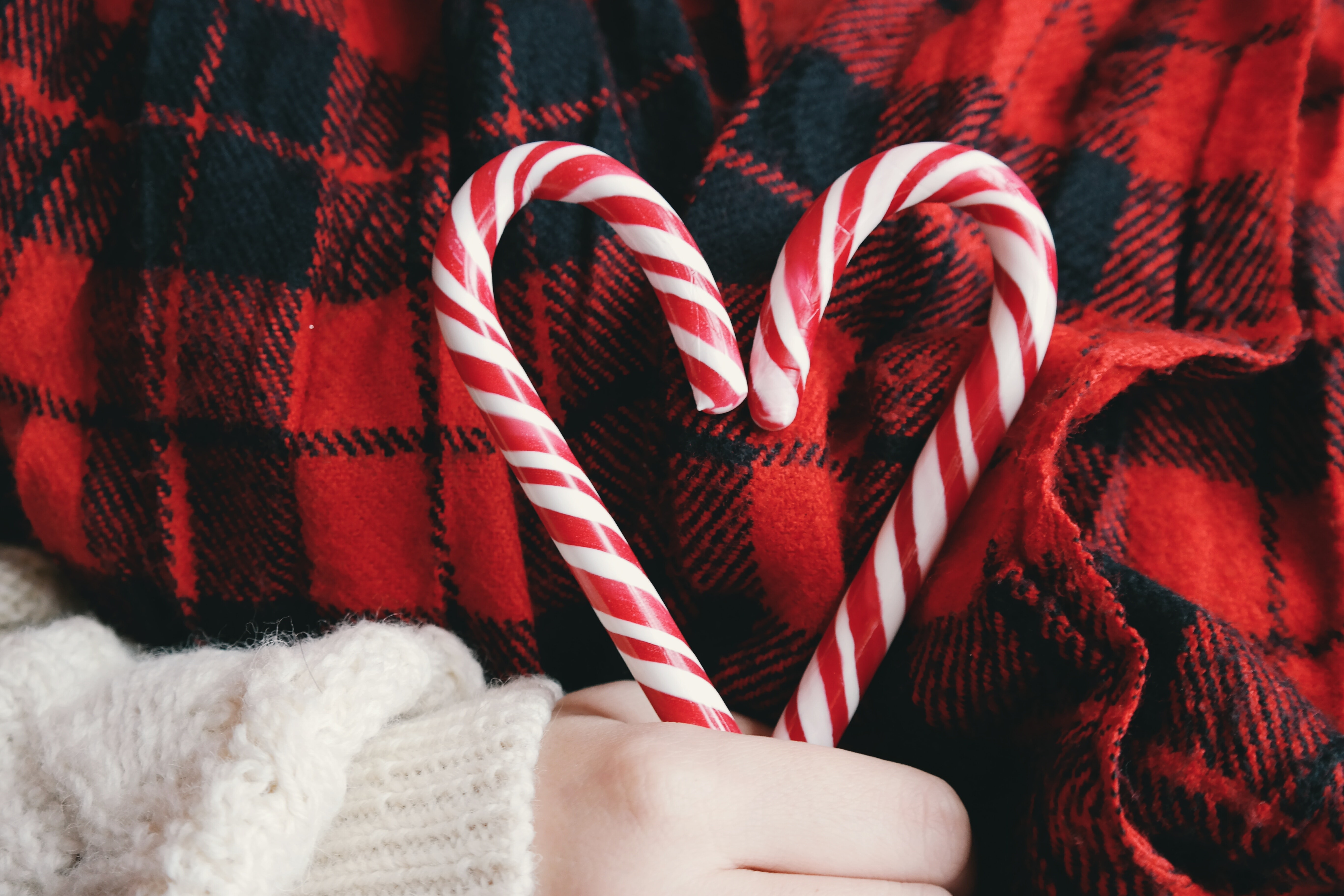 person holding candy cane heart with red and black plaid background